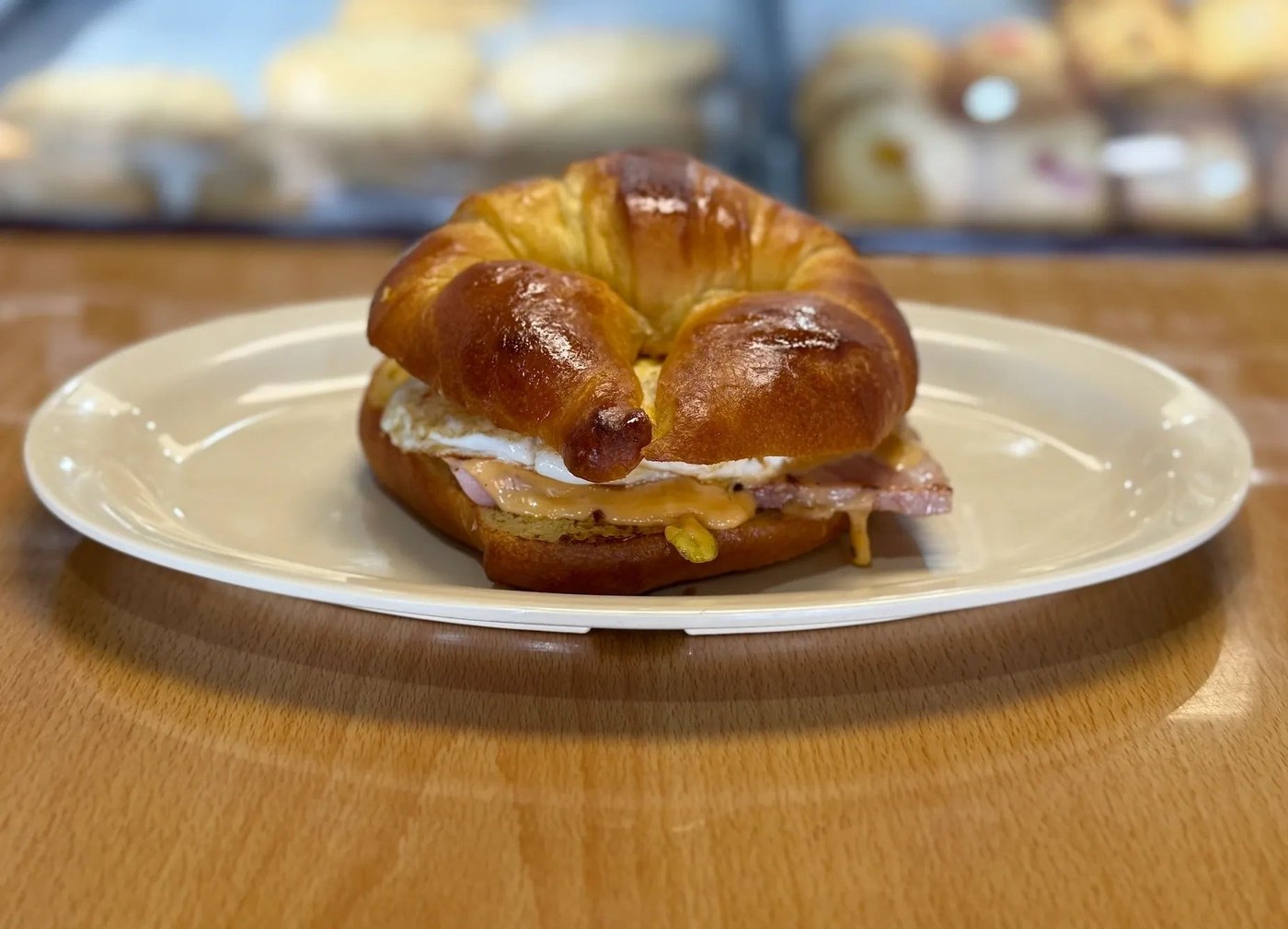 A glossy croissant breakfast sandwich with egg, ham and cheese on a plate at Lupita’s